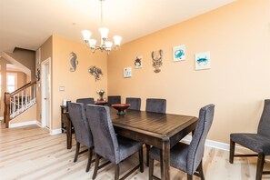 A dining area with a wooden table and grey upholstered chairs, a chandelier, and wall-mounted artwork.