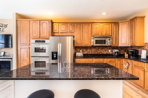 A kitchen with wooden cabinets, stainless steel appliances, a granite countertop, and a bar stool.