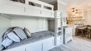 Una cama litera con escritorio y estanterías integradas, un comedor con sillas y una cocina con salpicadero de espiga.