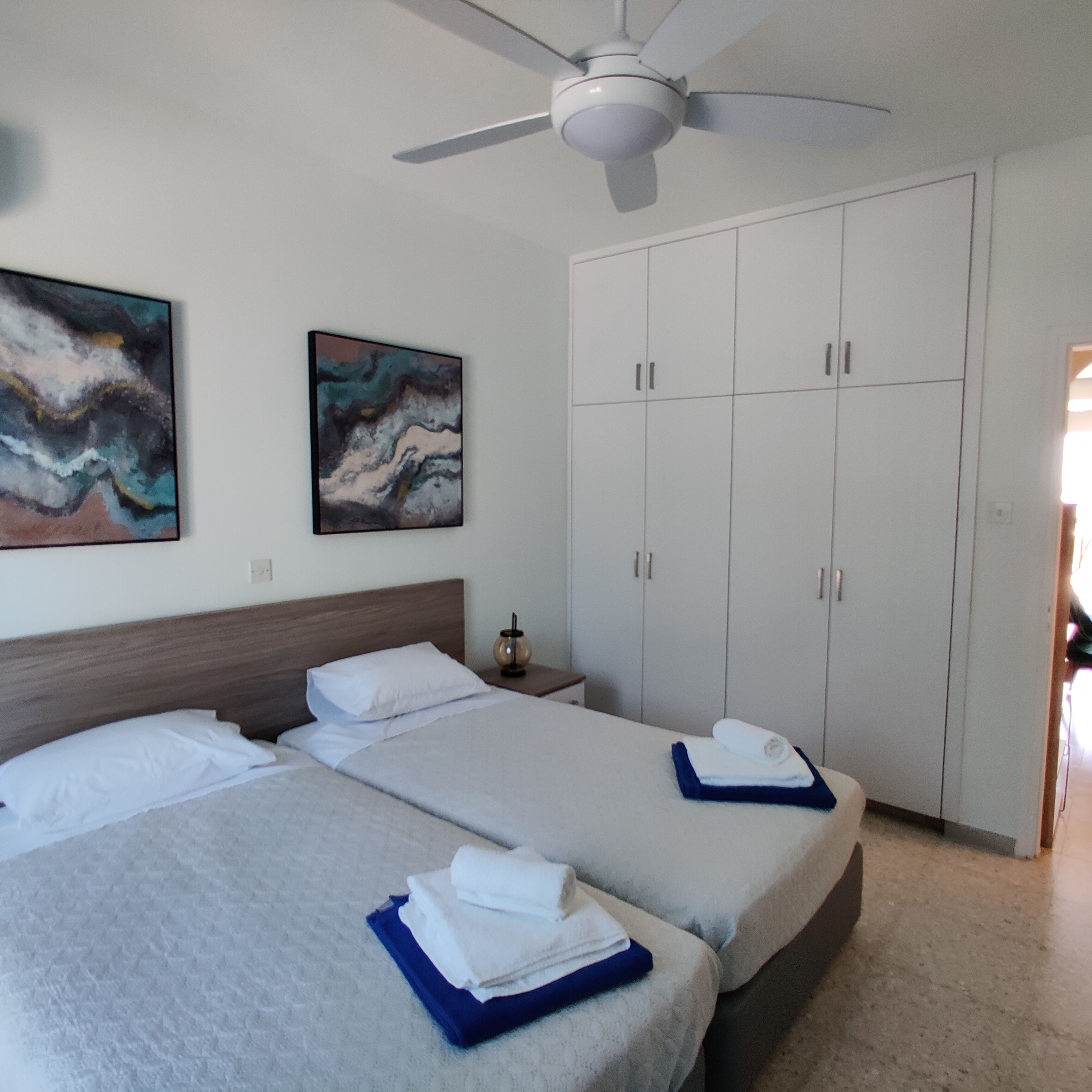 A hotel room with two beds, a wardrobe, and two abstract paintings on the wall.