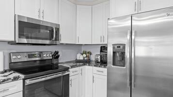 A modern kitchen with white cabinets, stainless steel appliances including a microwave, oven, and refrigerator, and a marble countertop.