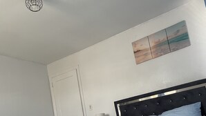 Een slaapkamer met een bed, nachtkastje, lamp en een plafondlamp.
