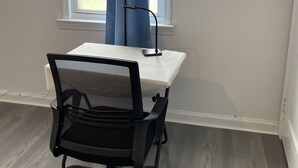 Een kleine kantoorruimte met een witte tafel, een zwarte bureaustoel en een raam met blauwe gordijnen.