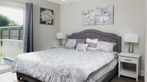 A bedroom with a large bed, two bedside tables with lamps, a grey upholstered headboard, and two floral paintings on the walls.
