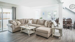 A modern living room with a sectional sofa, a coffee table, and a dining area with wooden chairs and a table. - New updated 1.5 blocks to beach, 5 min walk, 4 bedroom 3 bath, king size bed,  (Galveston)