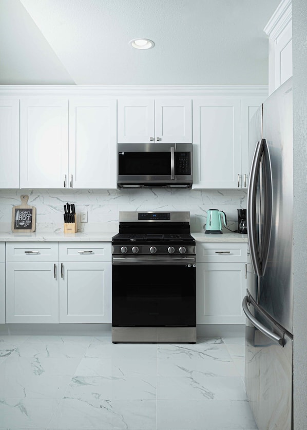 A modern kitchen with white cabinets, a stainless steel stove, a microwave, and a refrigerator.