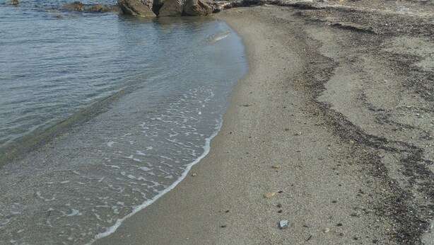 Een strand met helder water, rotsformaties en bergen in de verte.