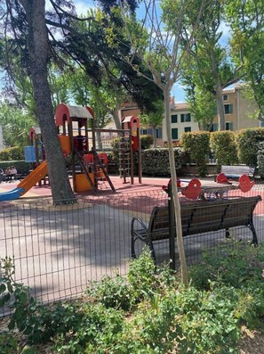 A playground with climbing structures and slides, surrounded by a fence and benches.