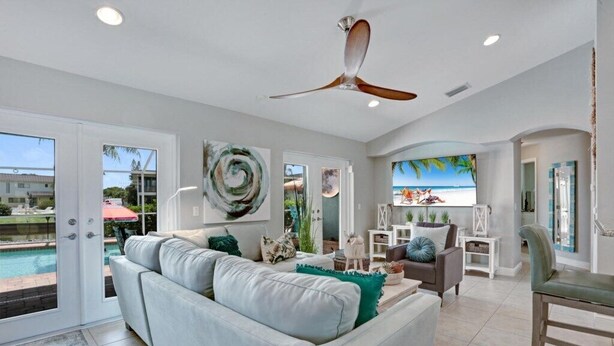 A spacious living room with a large white sofa, a ceiling fan, and a view of a swimming pool through glass doors.