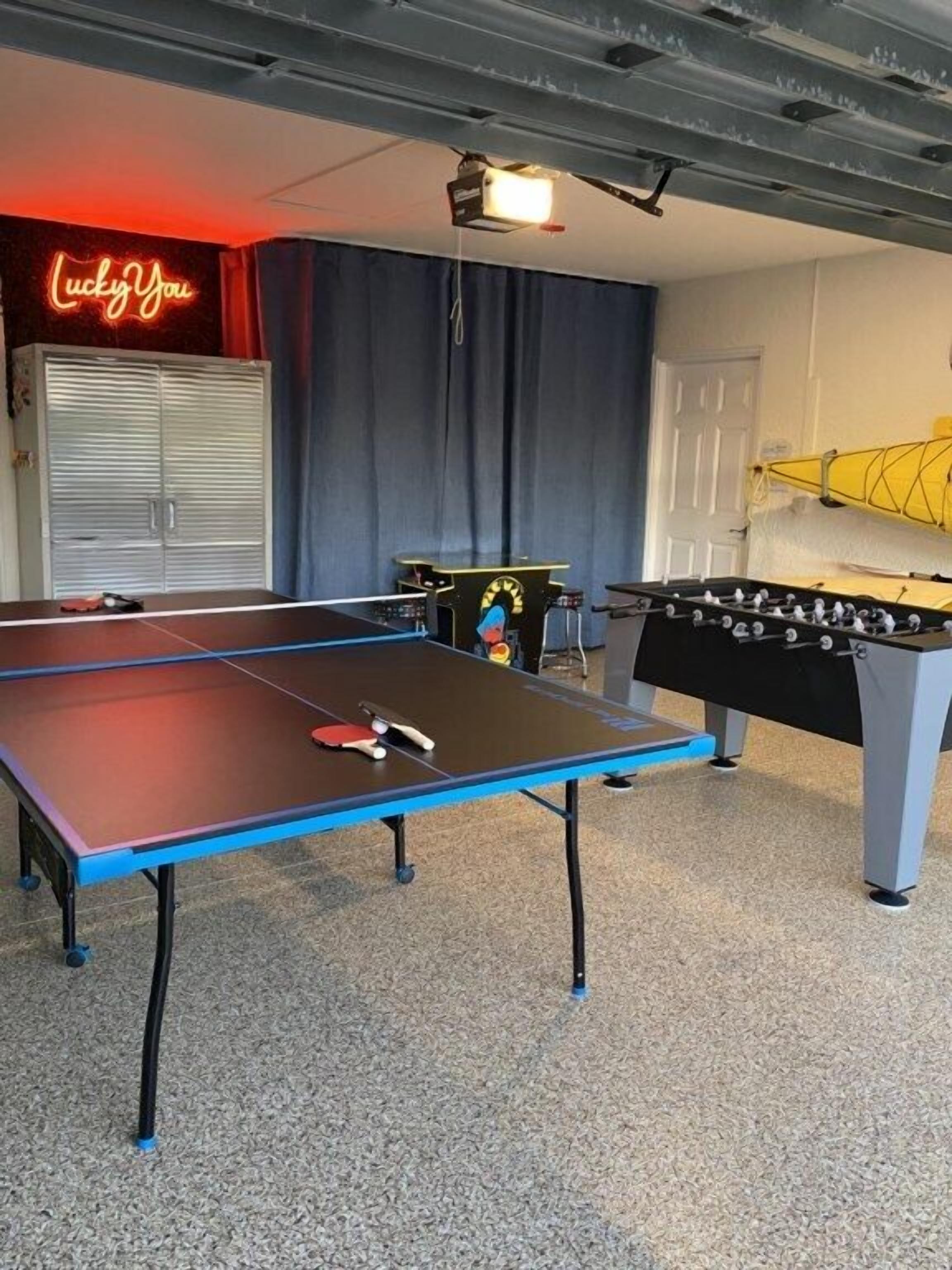 A room with a ping pong table, foosball table, and a neon sign reading "Lucky You".