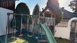 A backyard playground with a slide, swings, and a small wooden playhouse.