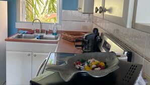 Pieni, käytännöllinen keittiö, jossa on pesuallas, liesi ja ikkuna, jossa on sälekaihtimet.