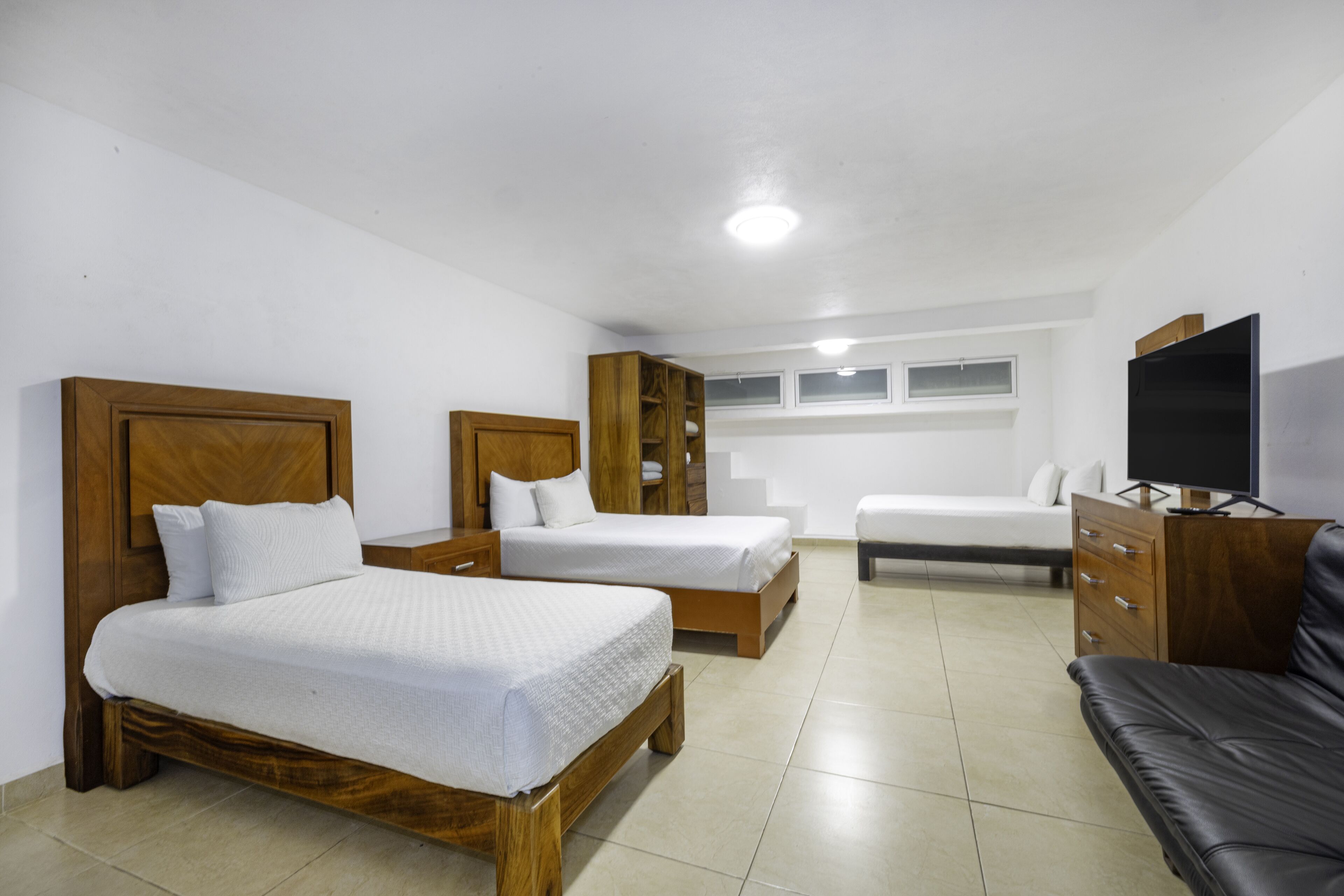 A hotel room with two wooden beds, a wooden wardrobe, a television, and a leather sofa.
