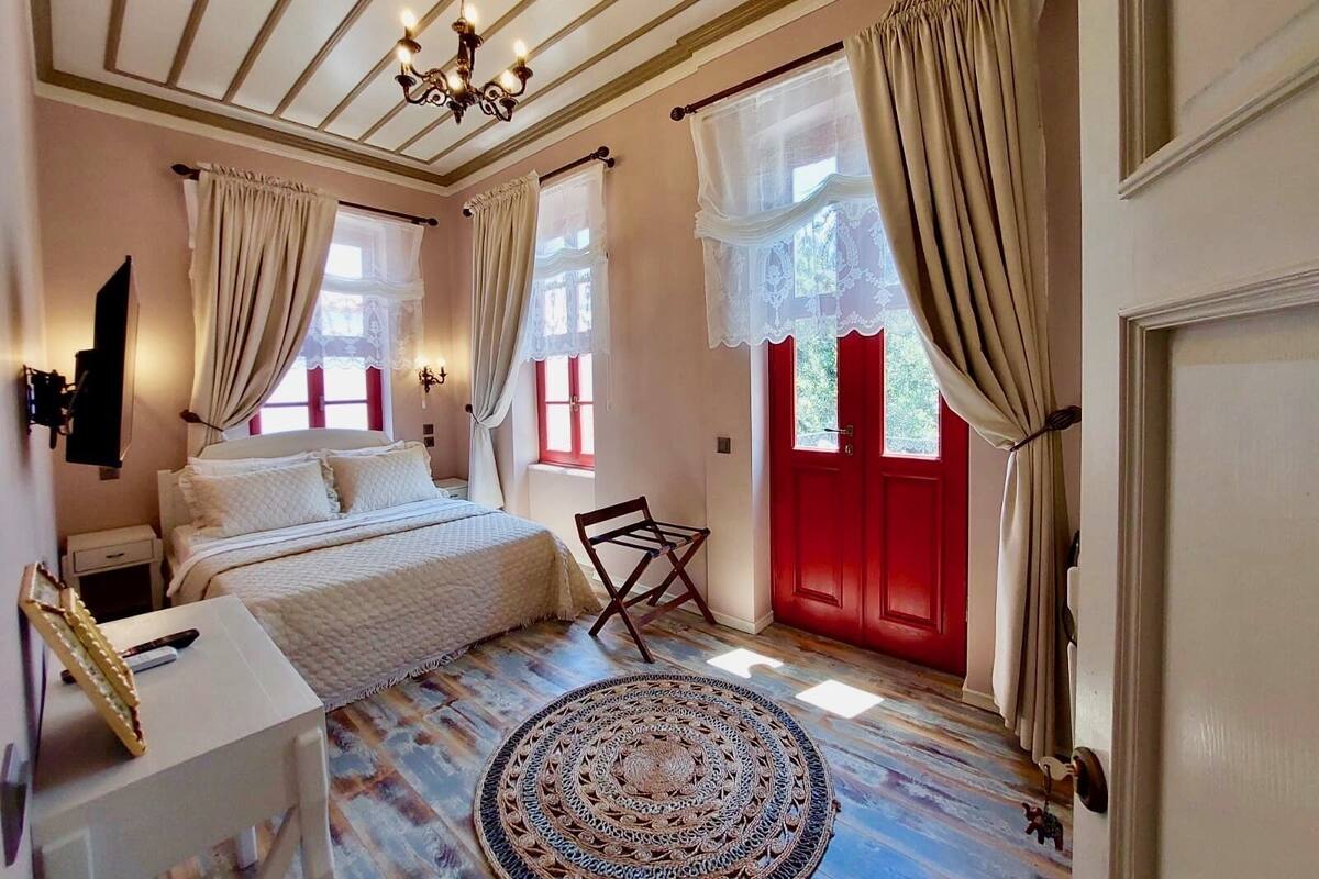 A bedroom with a bed, bedside table, lamp, and a red door.