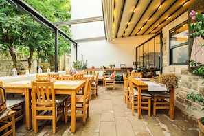 An outdoor patio with wooden tables and chairs, stone walls, and potted plants. - Corallia Ada Hotel (Bozcaada)