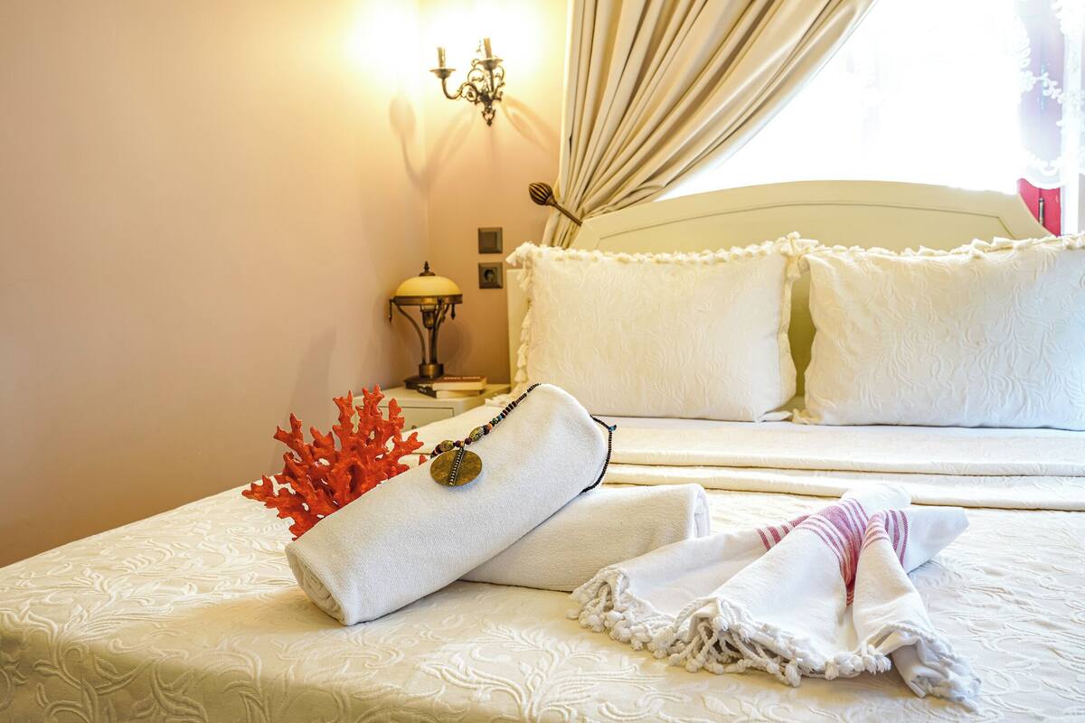 A neatly made bed with white linens and pillows, a decorative coral piece, and a lamp on a bedside table.