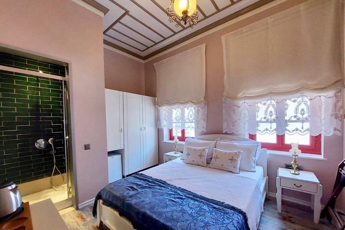 A bedroom with a bed, a wardrobe, a nightstand, and a window with lace curtains.