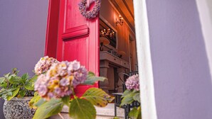 Una puerta roja con un adorno de corona, plantas en macetas y una escalera que lleva a una habitación.