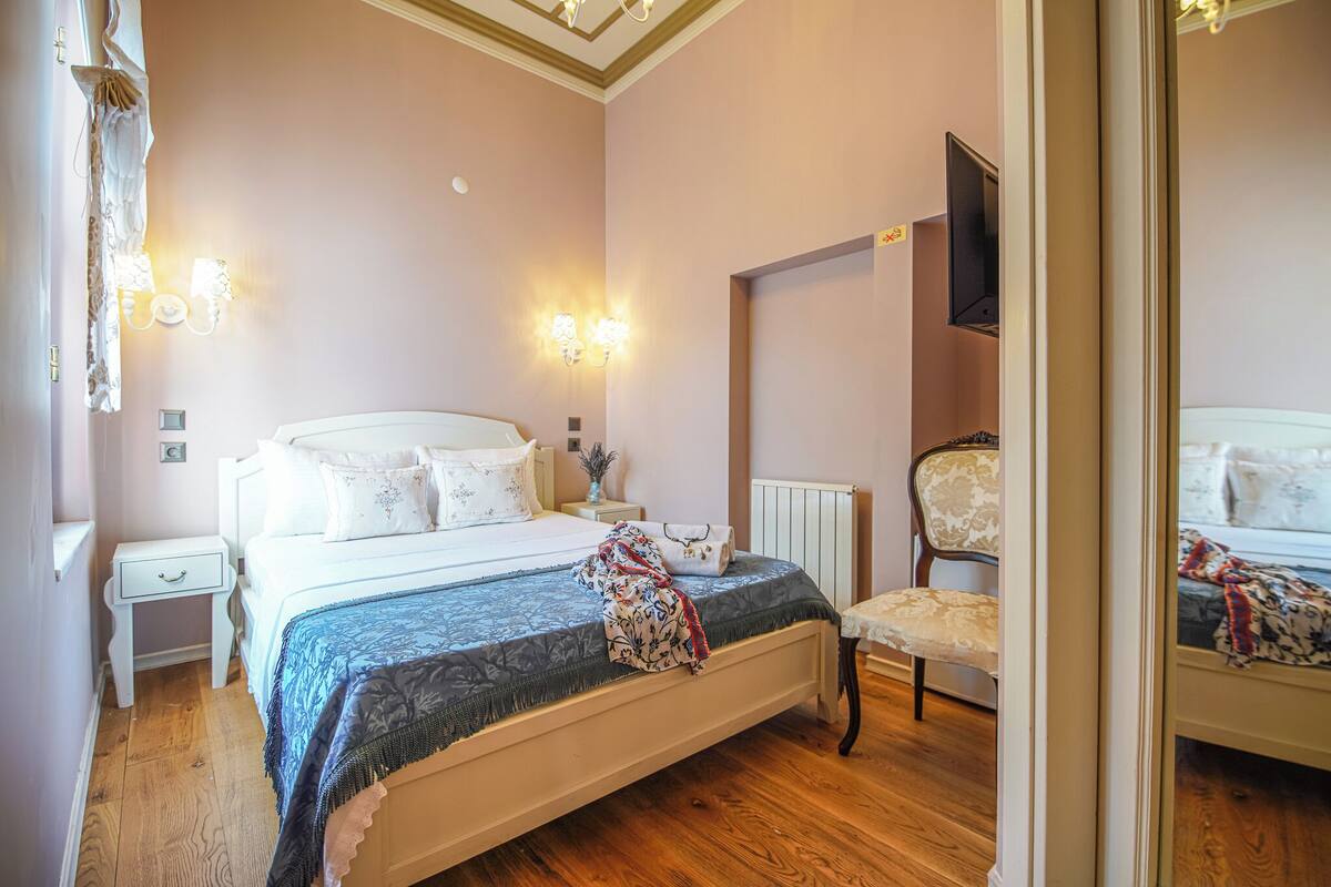A bedroom with a bed, bedside tables, a chair, a mirror, and wall sconces.