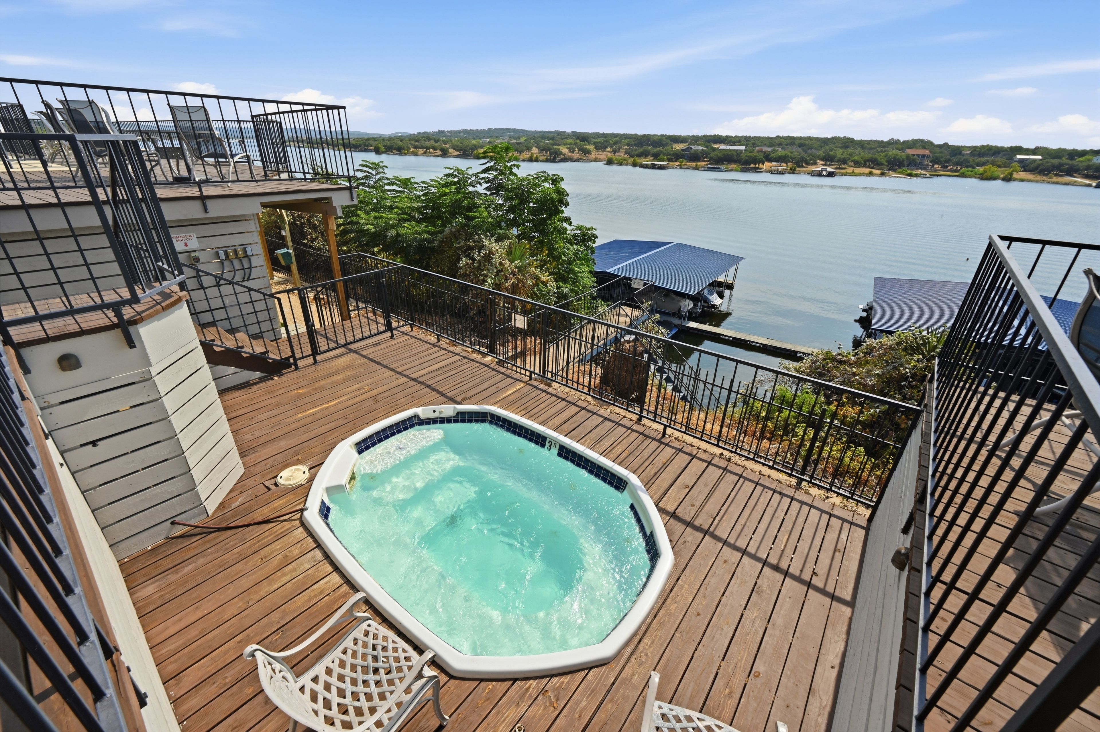 A hot tub on a wooden deck with a view of a lake and distant buildings.