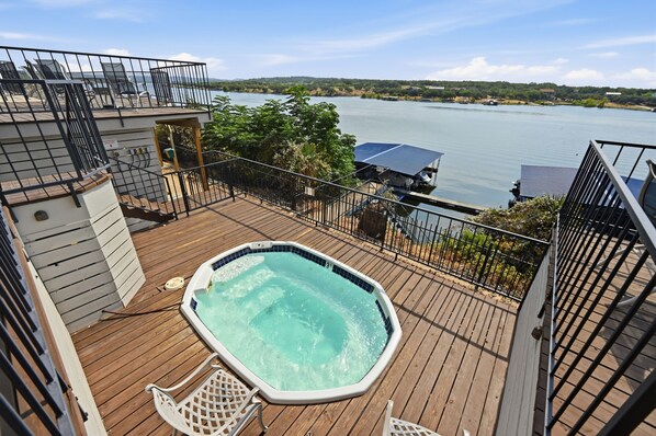 Un jacuzzi en una terraza de madera con vistas a un lago y edificios al fondo.