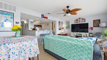 A compact living space with a dining area, a sofa, a television, and a ceiling fan.