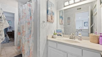 Ein Badezimmer mit Duschvorhang, Waschbecken, Spiegel und einem gerahmten Bild an der Wand.