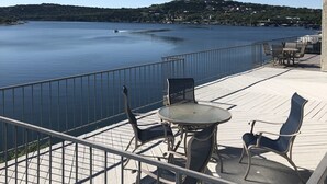 Une terrasse dotée de mobilier d’extérieur, offrant une vue sur une étendue d’eau paisible et une côte lointaine.