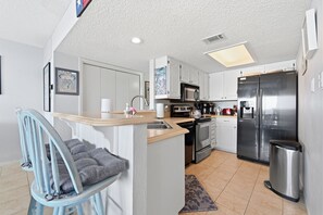 A modern kitchen with white cabinets, stainless steel appliances, and a blue chair. - Fun N Sun Lake Travis Waterfront Condo 104 Boat Slip Available (Spicewood)