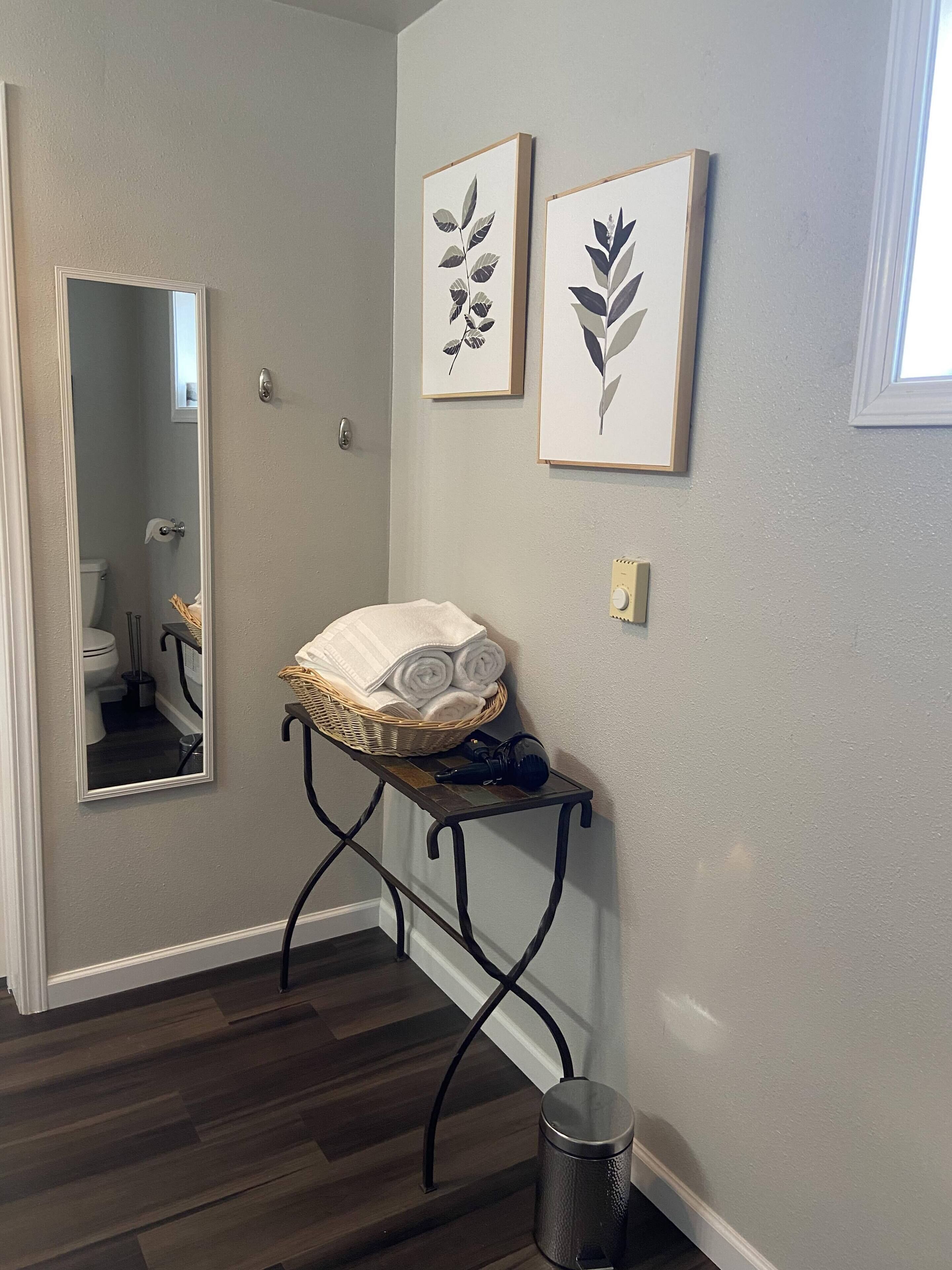 A hallway with a mirror, a small table with towels, and two framed leaf artworks on the wall.