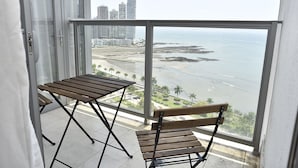 A balcony with a wooden table and chair, overlooking a beach and high-rise buildings. - Yoo Panama & Arts Tower (Panama City)