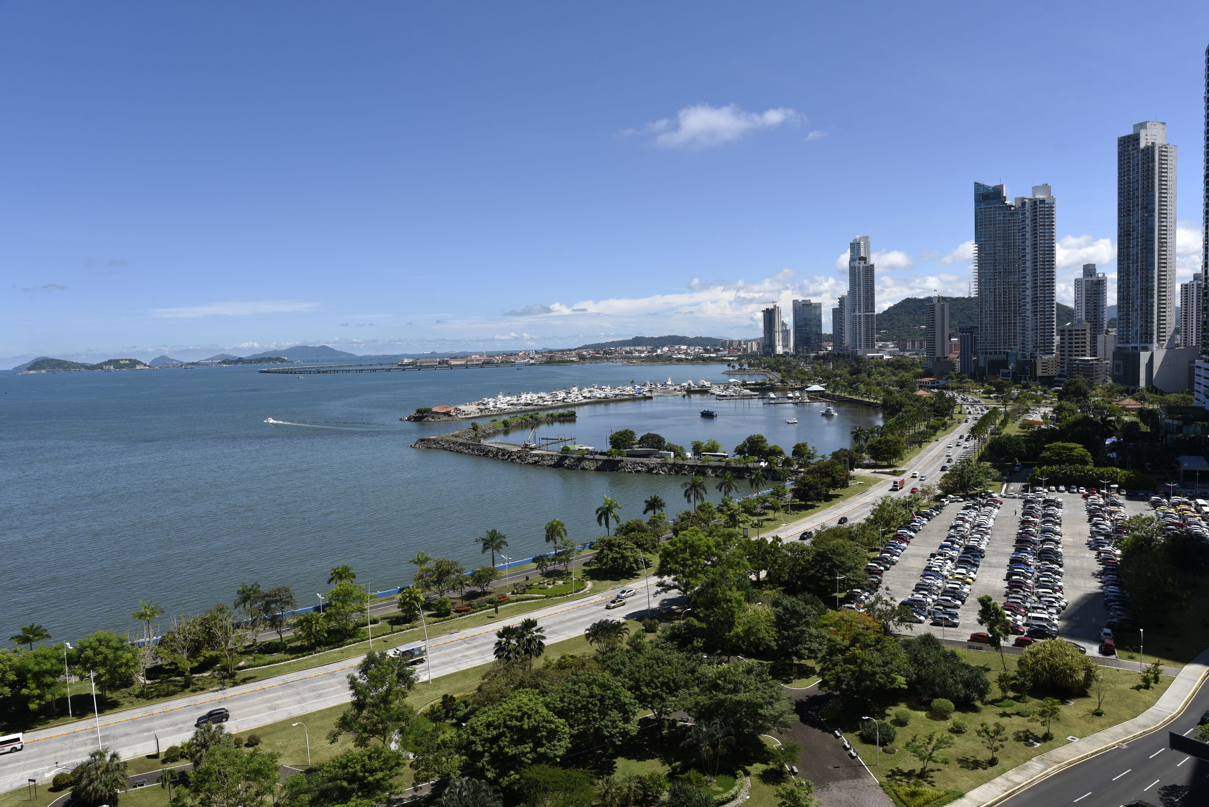 A coastal cityscape with high-rise buildings, a marina, and a parking lot.