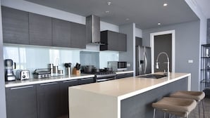 A modern kitchen with grey cabinets, stainless steel appliances, a central island with stools, and a built-in microwave. - Yoo Panama & Arts Tower (Panama City)