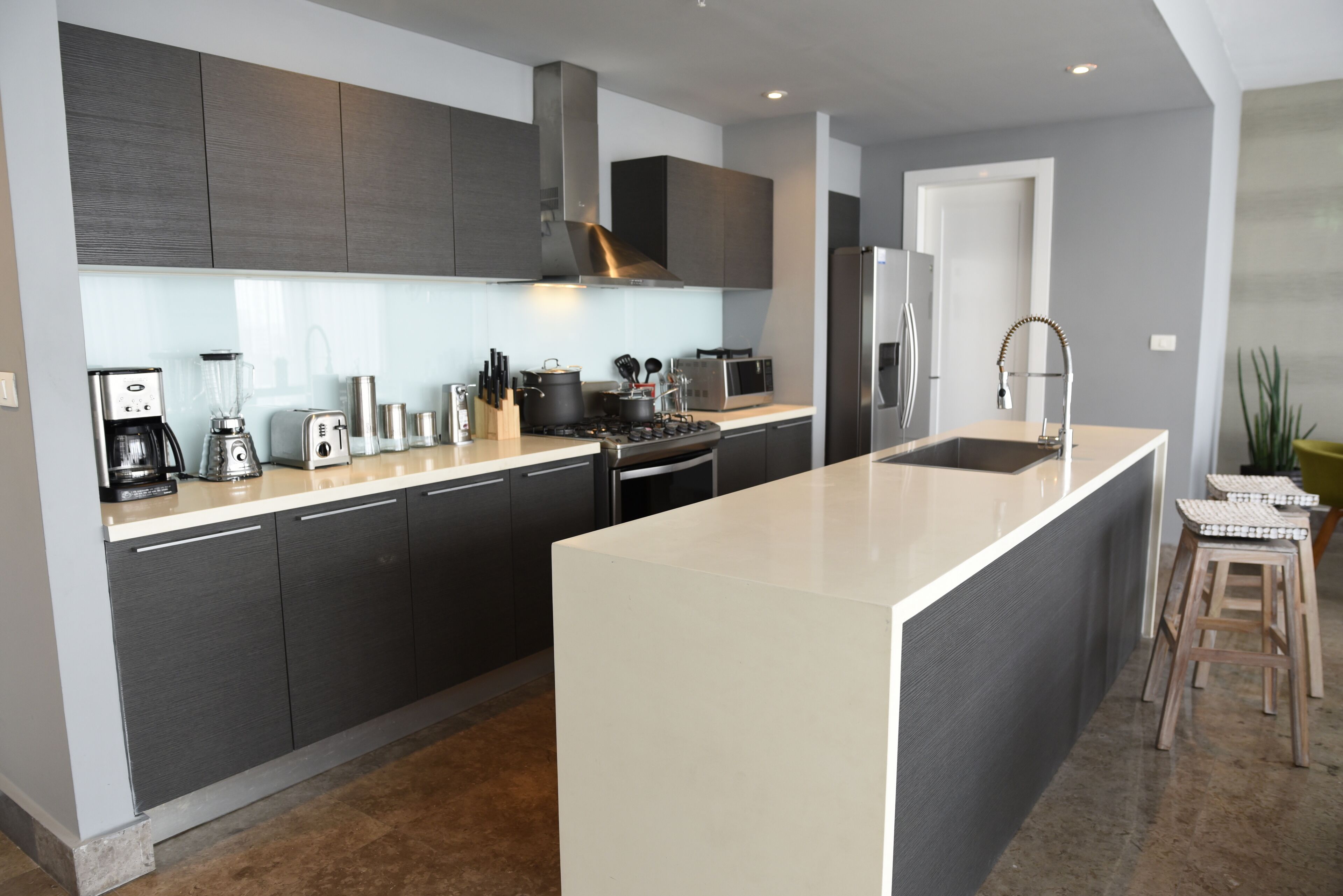 A modern kitchen with dark cabinets, a large island, and a stainless steel refrigerator.