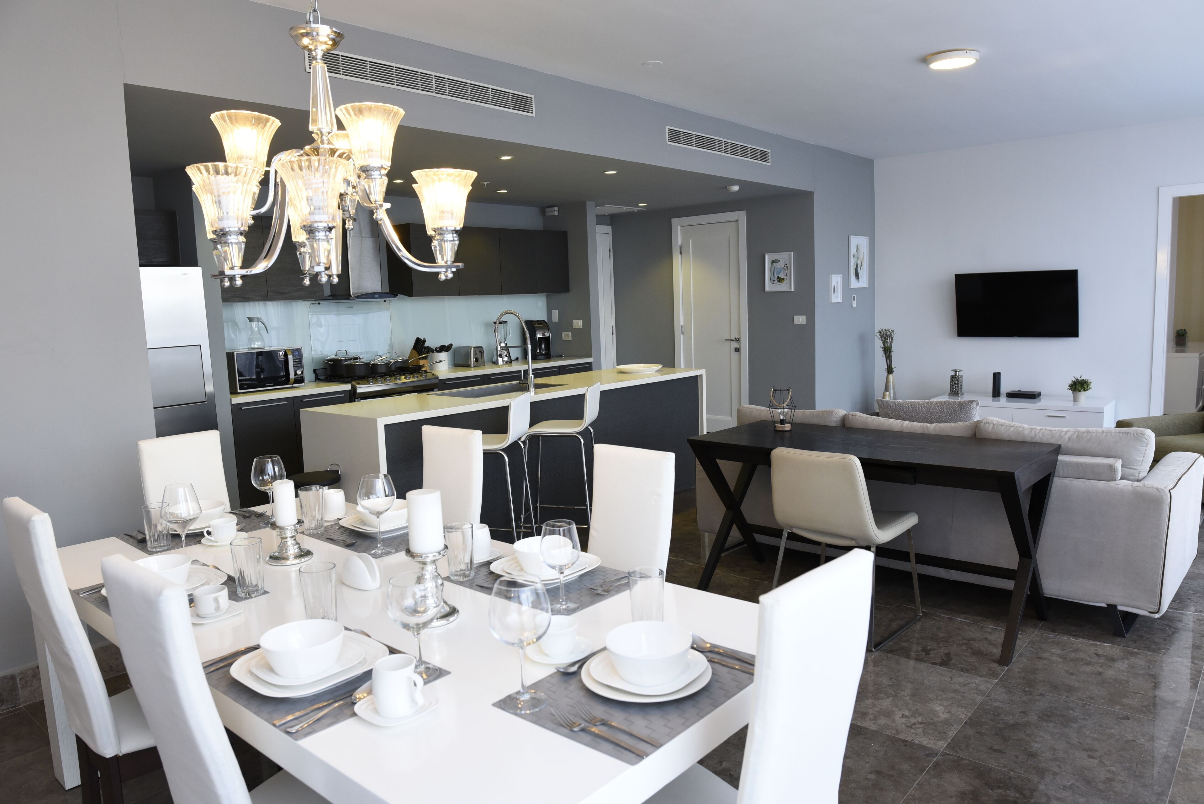 Una cocina moderna con comedor, muebles blancos y un televisor de pantalla plana.