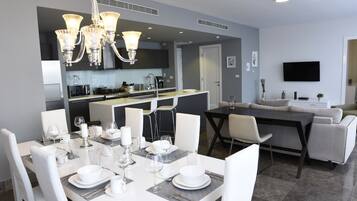 Una cocina moderna con comedor, muebles blancos y un televisor de pantalla plana.