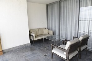 A balcony with a glass table, wicker chairs, a sofa, and a view of the sea through sheer curtains. - Yoo Panama & Arts Tower (Panama City)