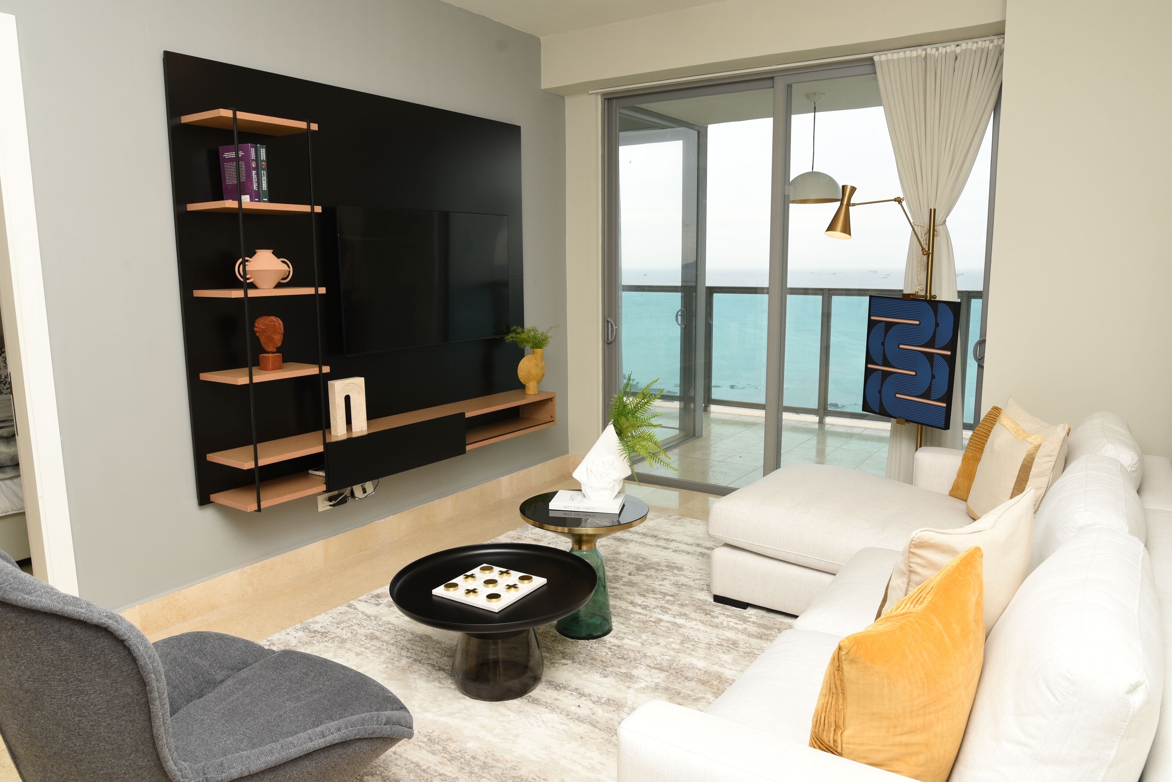 Una sala de estar moderna con una televisión de pantalla plana, un sofá, una mesa de centro y un balcón con vistas al mar.
