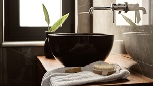 Une salle de bain avec un lavabo noir, un plan de toilette en bois, une serviette et une plante.