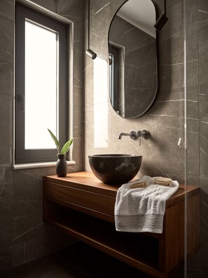 Une salle de bain moderne avec un grand miroir ovale, un meuble-lavabo en bois, un grand lavabo en forme de coupe, une serviette et une plante en pot.