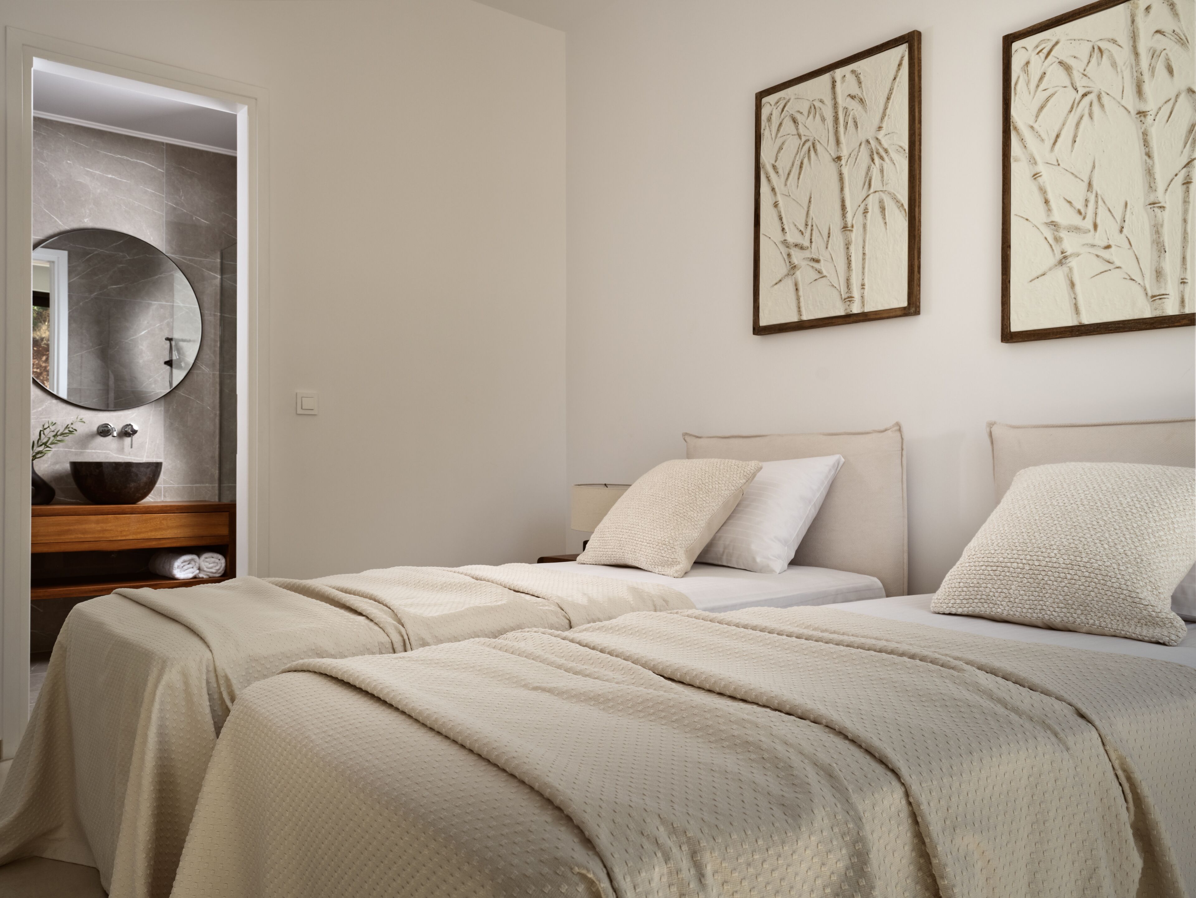 Ein Schlafzimmer mit zwei Betten, einem runden Spiegel, einem Holzschminktisch und zwei gerahmten Kunstwerken an der Wand.