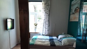 Un dormitorio con piso de madera, una cama con cubrecama a rayas, una ventana con cortinas y un televisor en la pared.