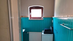Un baño estrecho con paredes verde azulado, una ventana, un radiador y una lavadora pequeña.