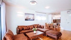 A modern living room with a brown sectional sofa, a wooden coffee table, and a dining area with wooden chairs and a table. - Deluxe Apartment Isabela Prague (Zadar)