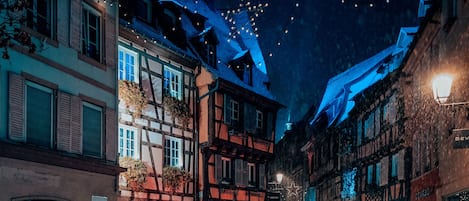 En smal gata kantad av traditionella hus med korsvirkesfasader, varav några har synliga skyltar och butiksvitriner.