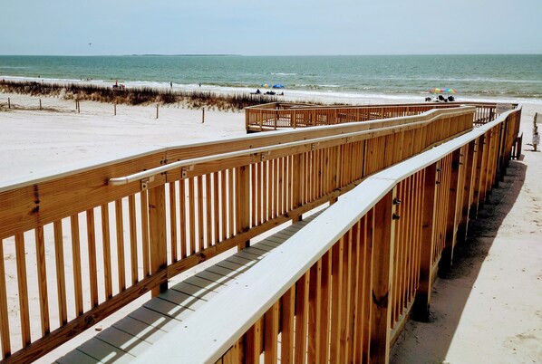 A wooden boardwalk leading to a sandy beach with a view of the ocean.