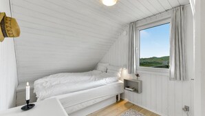 A bedroom with a single bed, a bedside table, a nightstand, a window with curtains, and a view of the outdoors. - Beautiful home in Hvide Sande with WiFi (Hvide Sande)