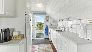 A narrow kitchen with white cabinetry, a built-in oven, and a large window leading to a view of the outdoors. - Beautiful home in Hvide Sande with WiFi (Hvide Sande)