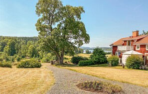 Traditional house with a classic architectural style, set amidst a serene countryside landscape with a tree-lined pathway and open fields.