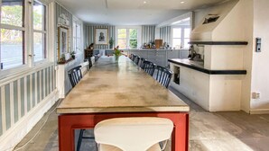 A long dining table with chairs, a kitchen area with a countertop, and a view of the outdoors through large windows. - 3 bedroom beautiful home in Hovås (Hovås)